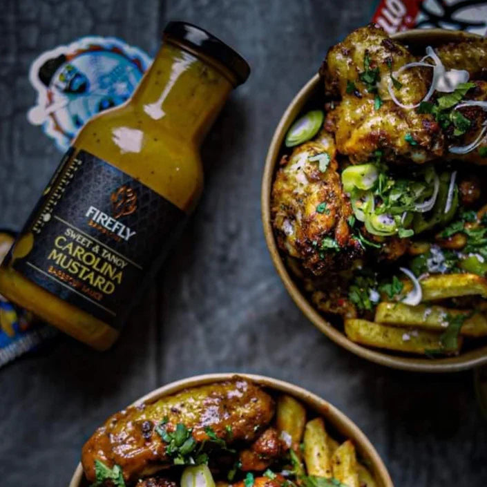 Bowl of food with a bottle of Firefly Barbecue Sweet & Tangy Carolina Mustard on a dark surface.