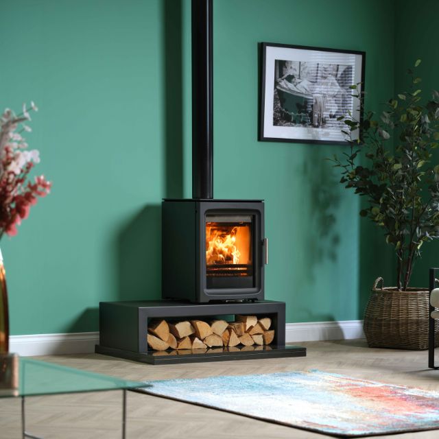 Wood-burning stove in a room with green walls, a plant, and a picture frame.