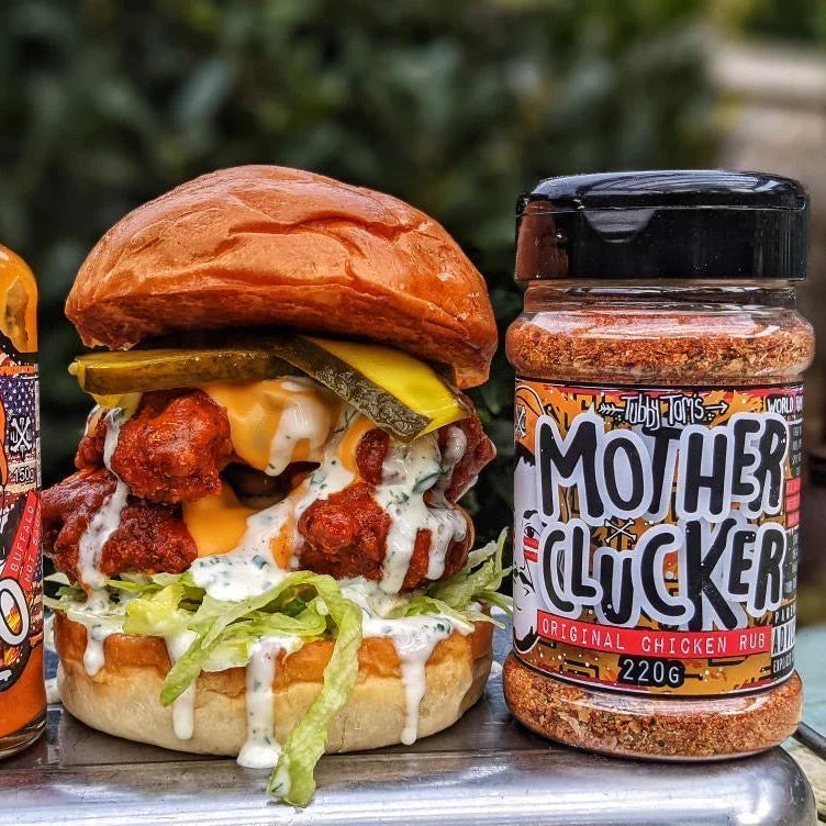 Chicken Burger with toppings and a jar of 'Mother Clucker' seasoning on a metal surface.