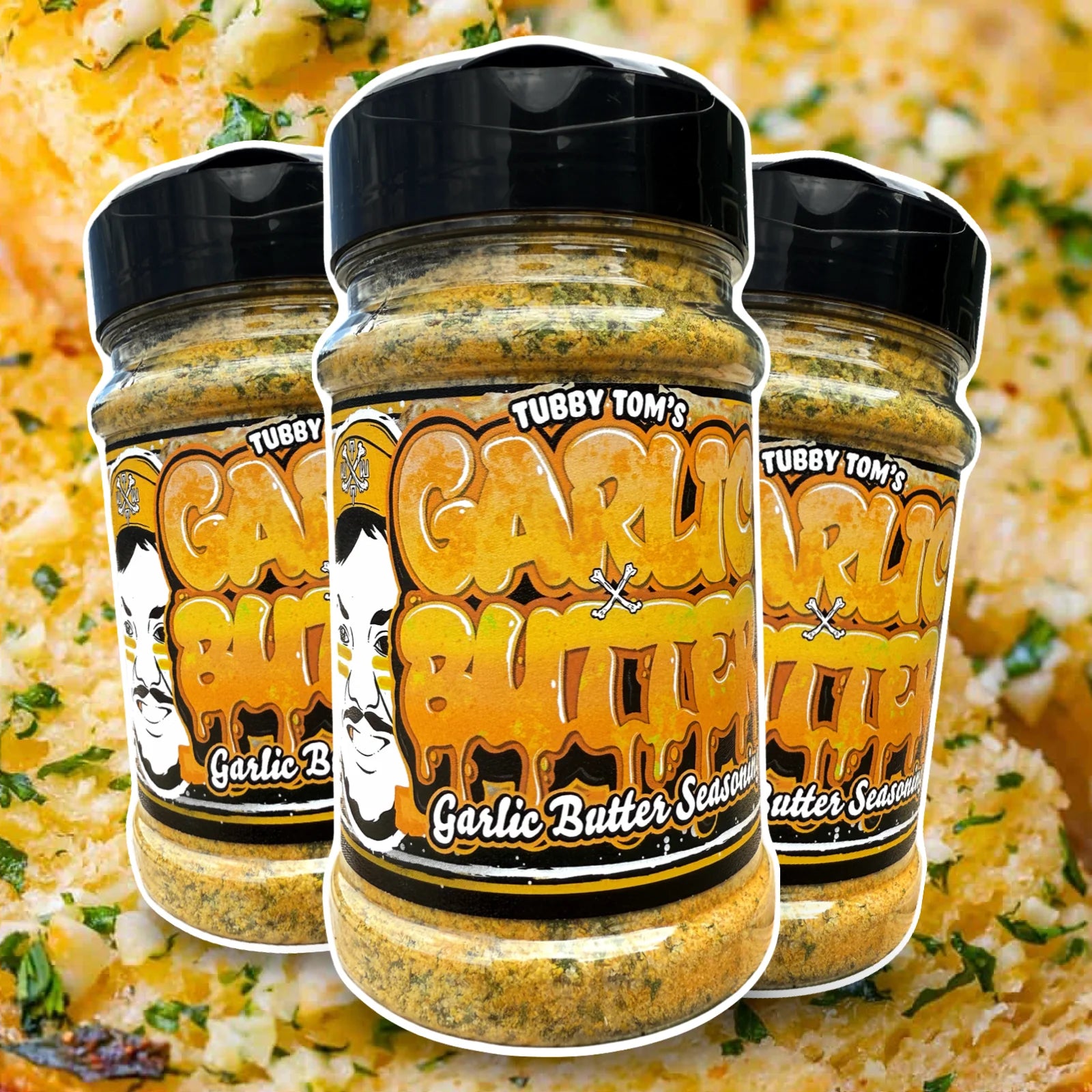 Three jars of Tubby Tom's Garlic Butter seasoning on a blurred background of a dish.