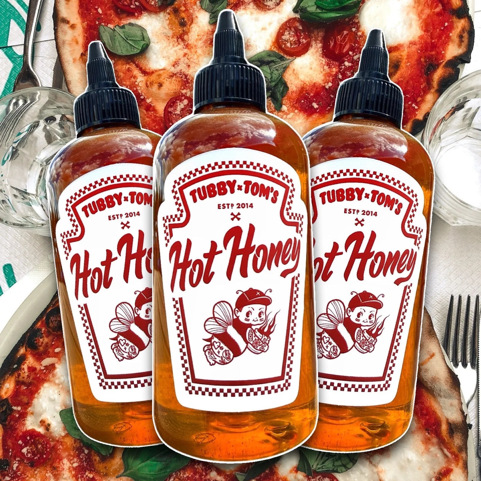 Three Tubby Tom's Hot Honey Bottles displayed in front of a pizza background