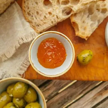 Assorted tapas including bread, olives, and a small bowl of red spread on a wooden board.