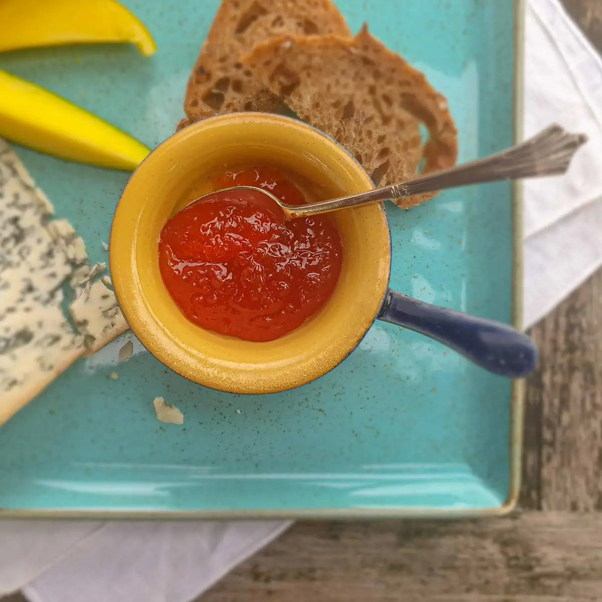 Yellow bowl with red jam on a blue plate with bread and bananas