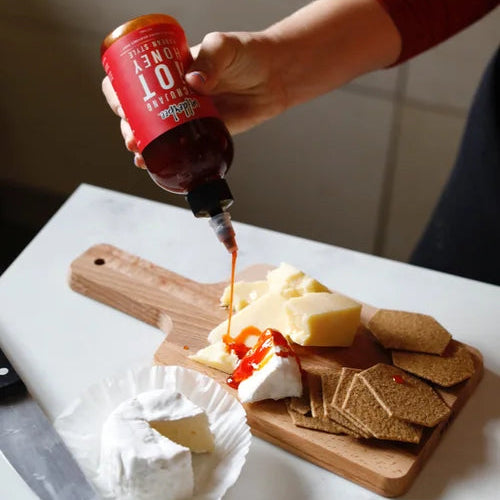 Person drizzling WilderBee hot honey from a bottle onto a cheese board
