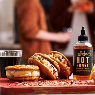 Two ice cream sandwiches with a bottle of WilderBee hot honey on a wooden board