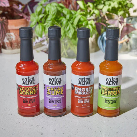 Four bottles of 'Eaten Alive' hot sauces on a surface with plants in the background