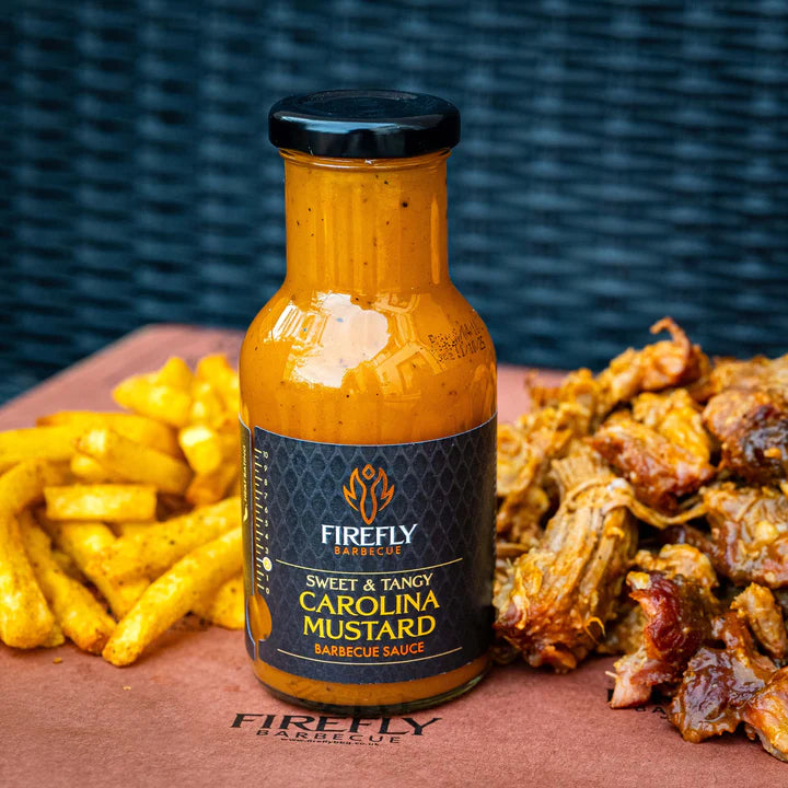 Bottle of Firefly Barbecue Sweet & Tangy Carolina Mustard Barbecue Sauce with fries and pulled pork on a wooden board.