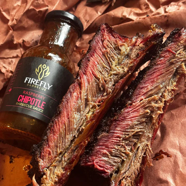Bottle of Firefly Raspberry Chipotle Barbecue Sauce next to sliced smoked meat on butcher paper.