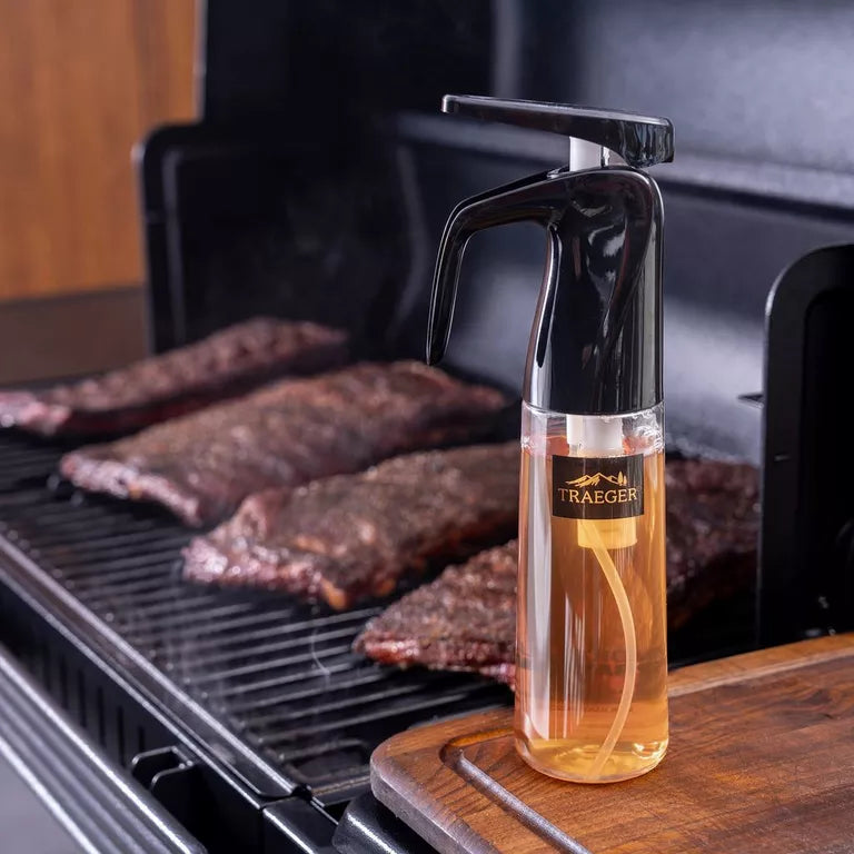 Bottle of Traeger wood-smoke cooking liquid on a grill with cooked steaks.