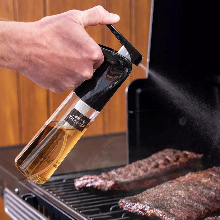 Person using a bottle of Traeger wood-smoke syrup on ribs on a grill.