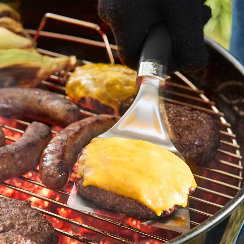 Grilled cheeseburger being held over a grill with sausages.