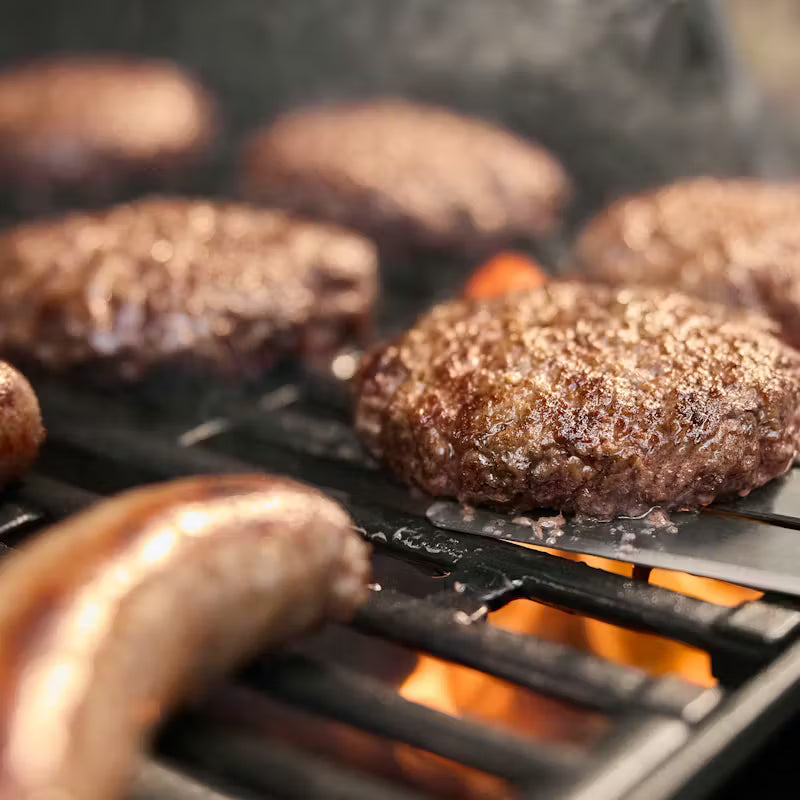 Hamburgers and sausages cooking on a grill with flames in the background